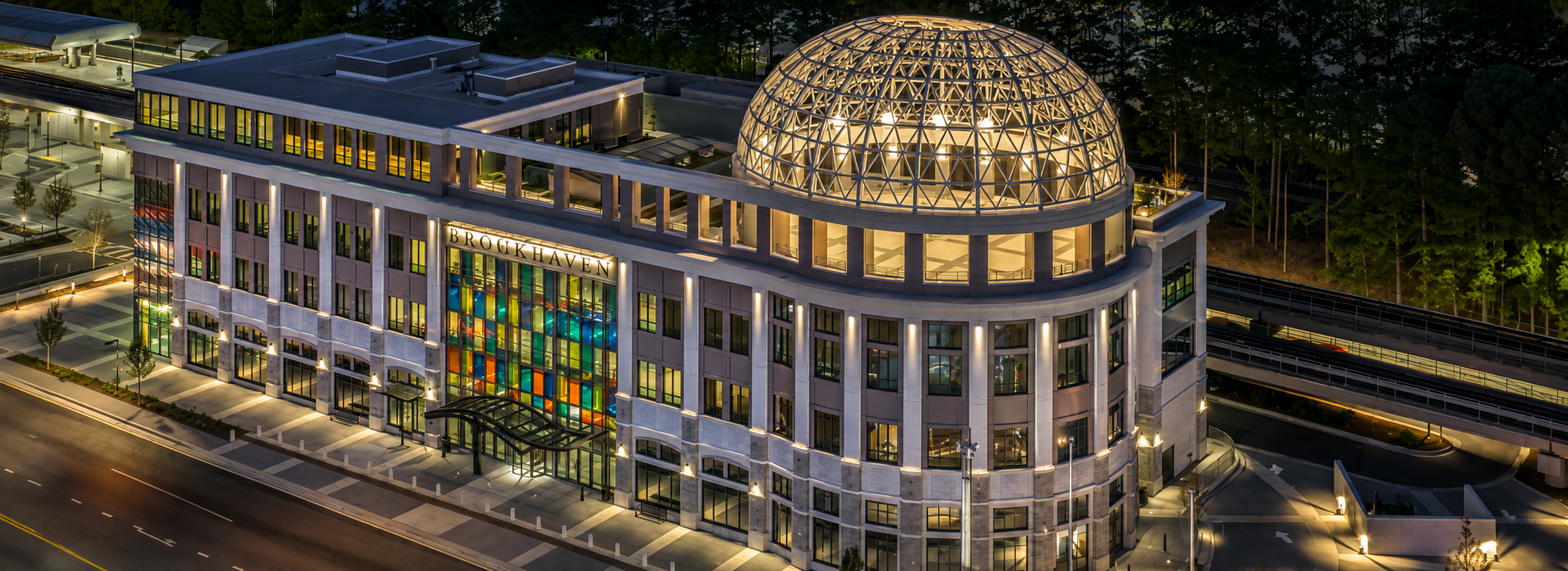 Aerial night view of a modern office building with a glass dome and BROOKHAVEN signage, next to the Brookhaven/Oglethorpe MARTA station